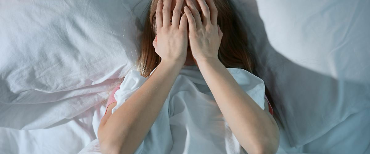 woman laying in bed holding her face suffering from insomnia